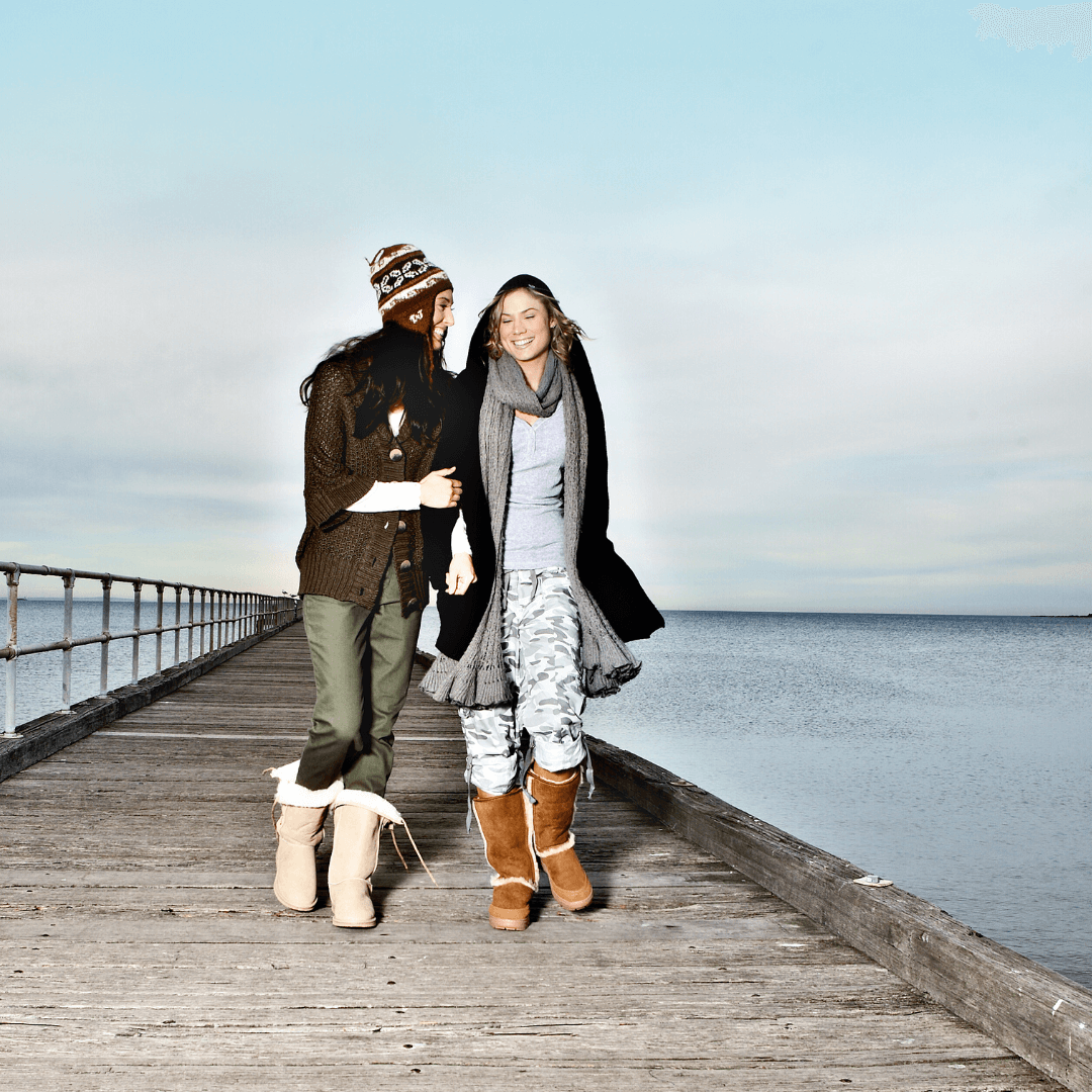 Two women arm in arm walking along Melbourne pier dressed in winter gear and Ugg Boots